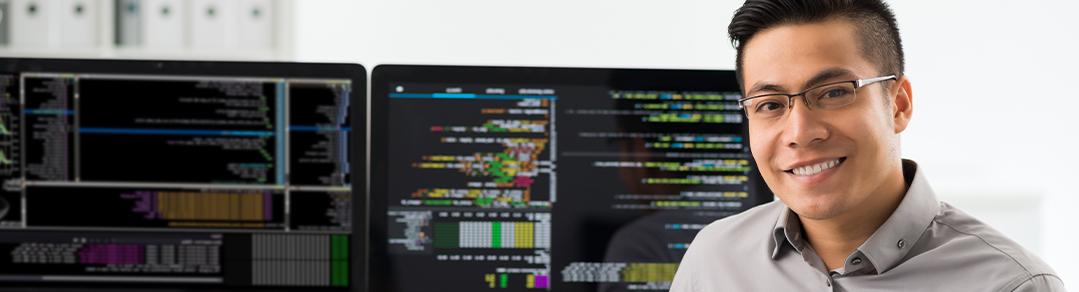 一个男人坐在两个电脑屏幕前，两个屏幕上都有编程语言